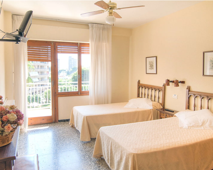 Vista genreal de la habitación, con balcón al fondo y camas separadas con cubrecamas de color crema