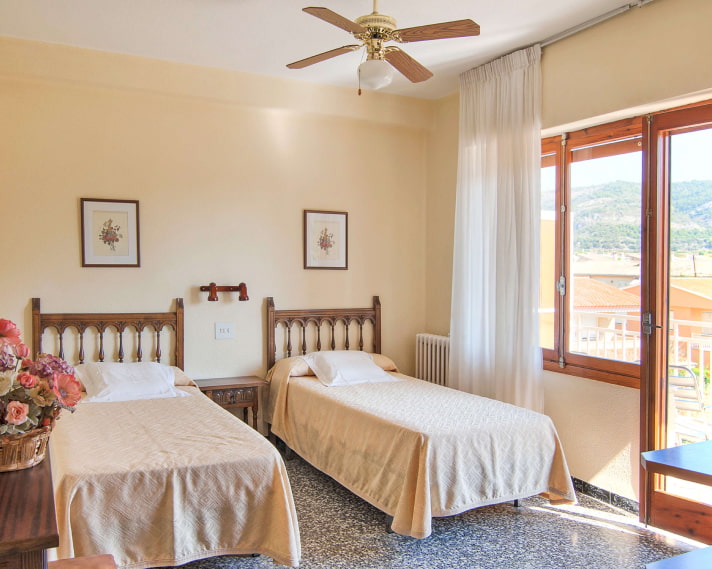 Nueva perspectiva de la habitación, con balcón al fondo y camas separadas con cubrecamas de color crema